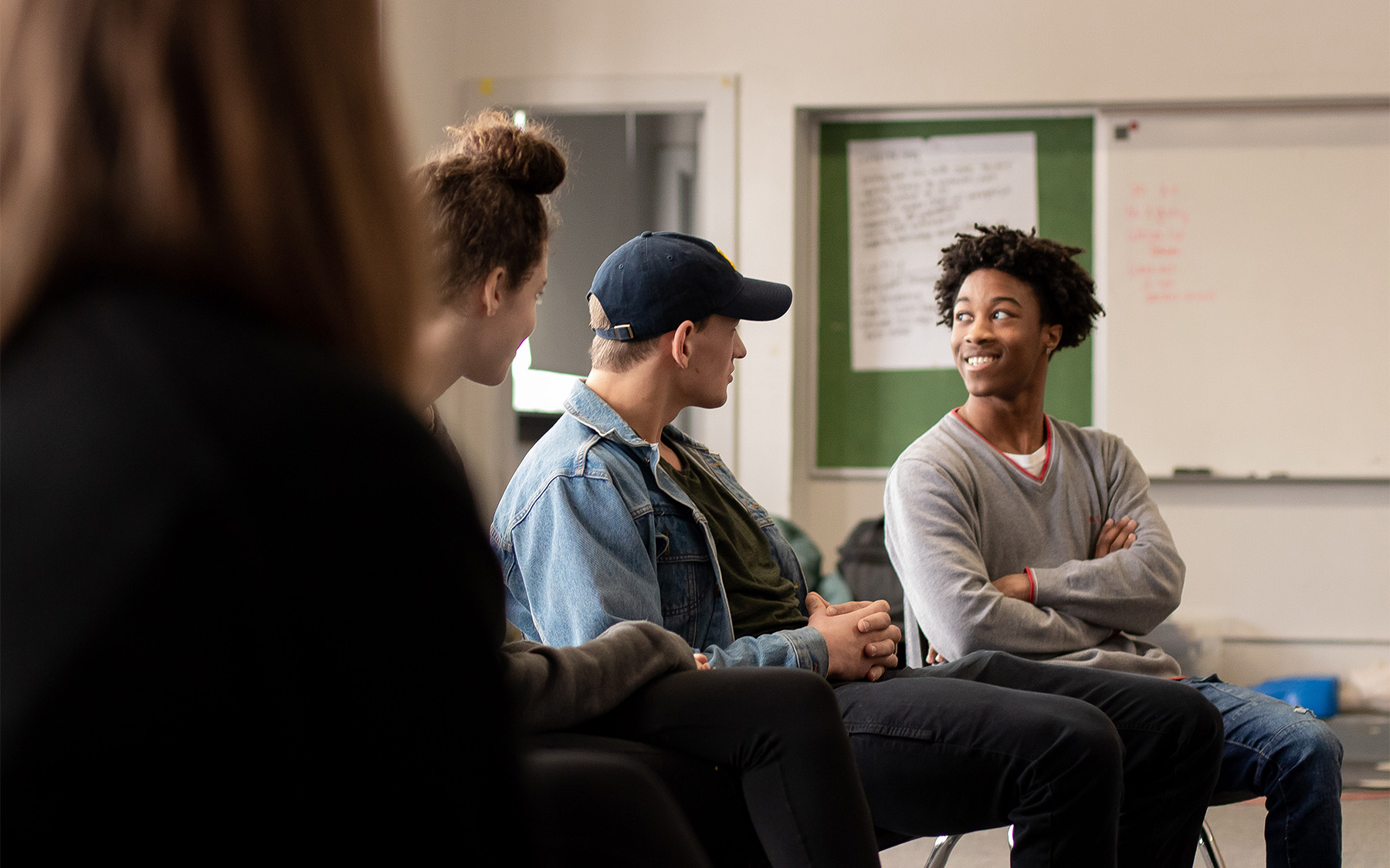 three high school students sitting in a row and talking with smiles on their faces