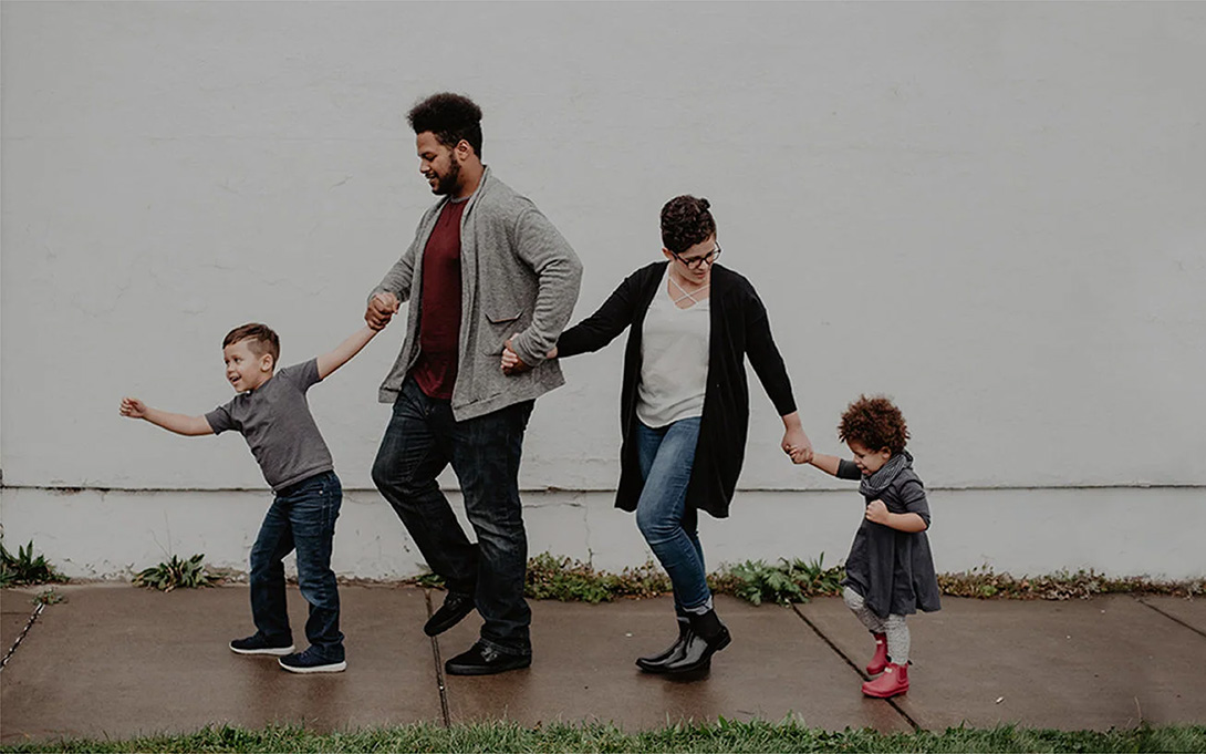 a family of 4 holding hands and walking happily in a line on the pavement