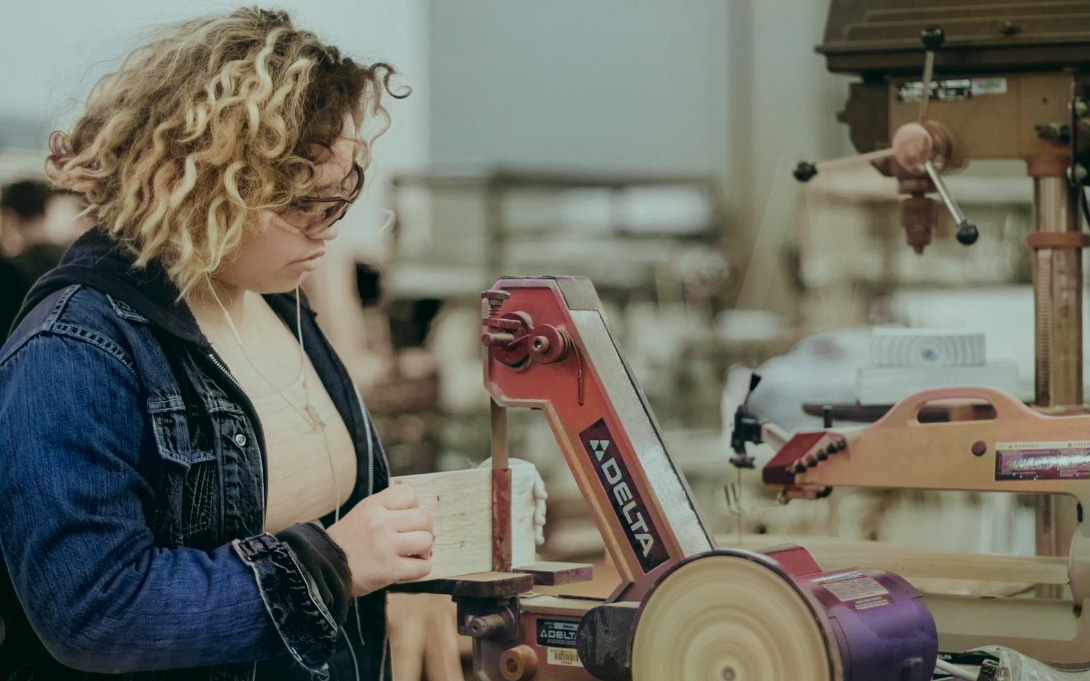 a student cutting a piece of wood board with a power tool