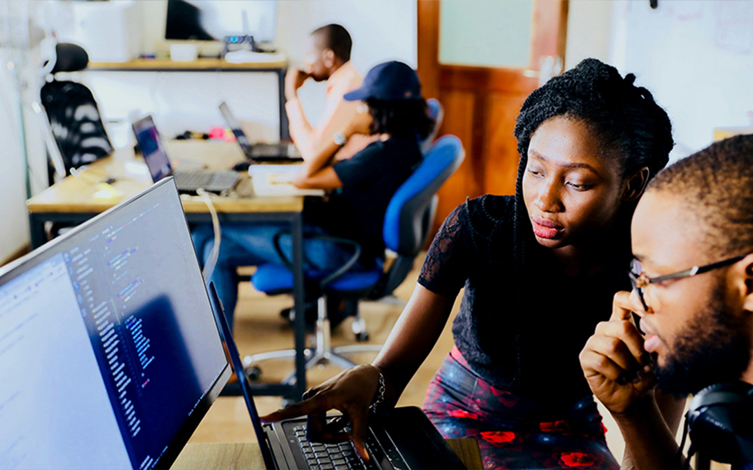two high school students walking in front of a classroom computer