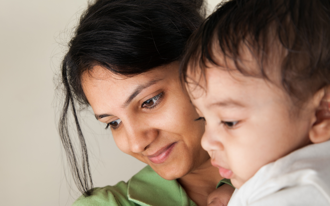 Mom holding baby and smiling as they look at something 
