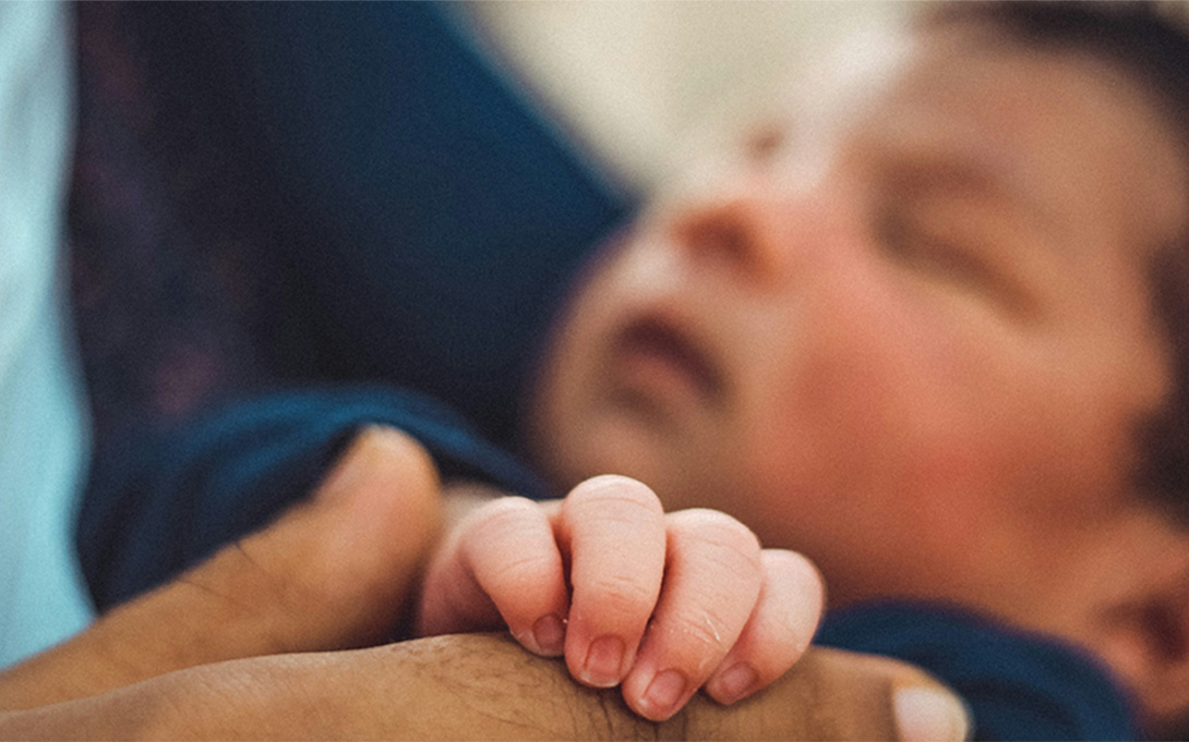 an infant's hand holding the fingers of an adult