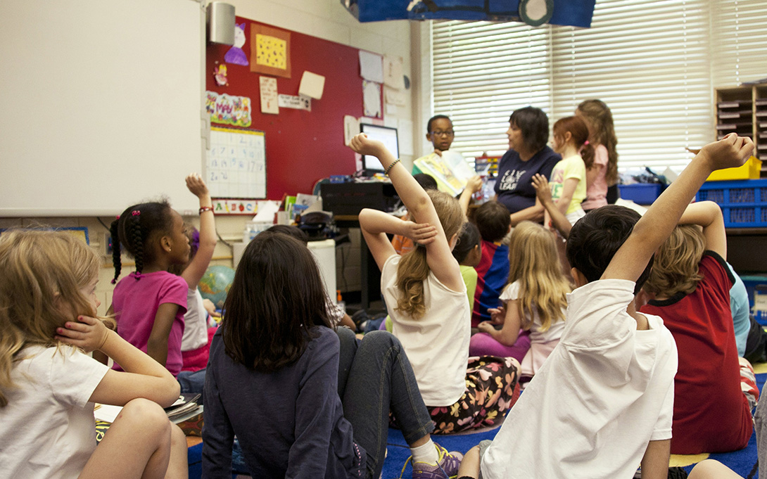 a teacher giving whole class instructions with three students by her side in an elementary classroom