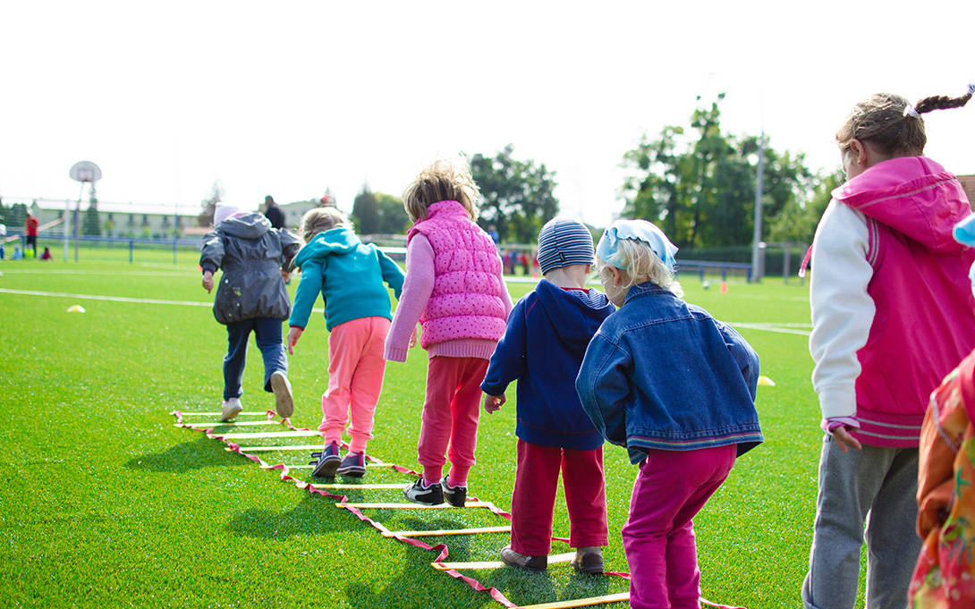 a row of young children jumping on the playground's green grass.