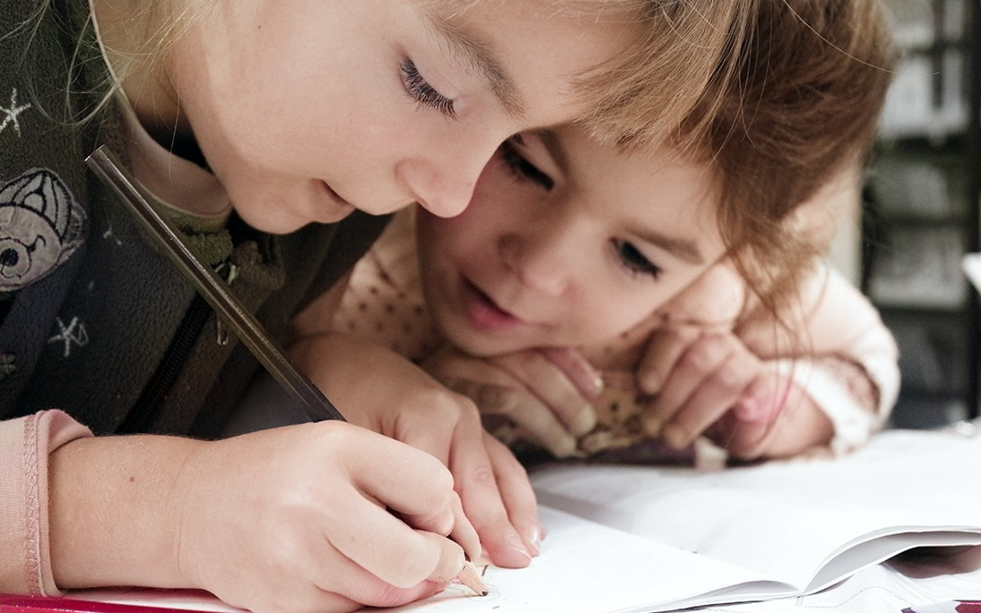 two elementary students writing on a notebook