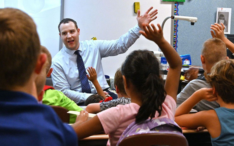 Teachers talking to students with their hands up in the classroom