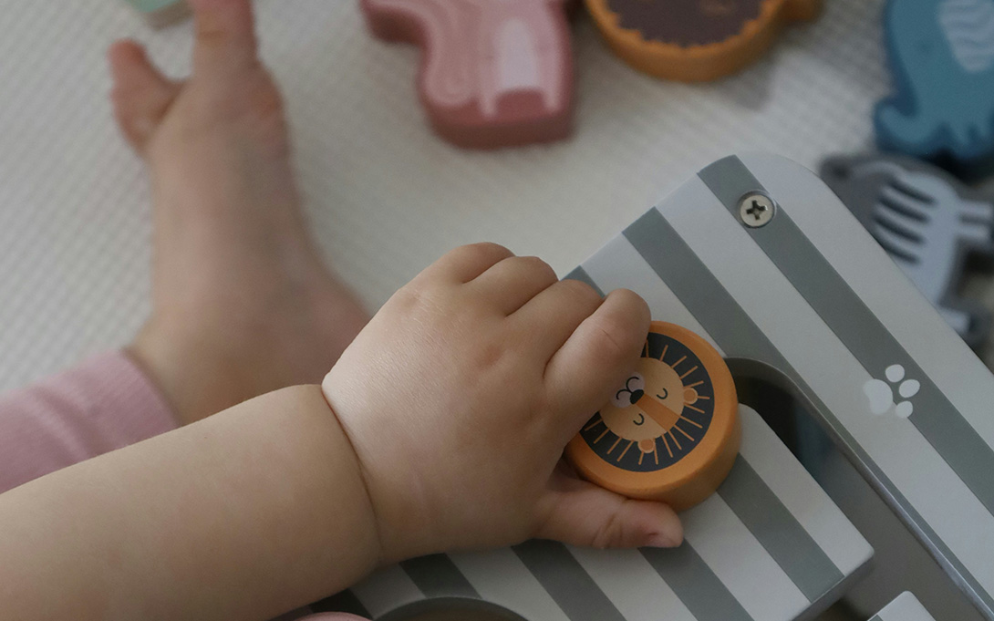 a photo of a baby's bare hand and foot on the floor mat playing with a wooden toy