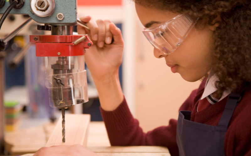 Student with safety goggles operating a machinery with a drill bit
