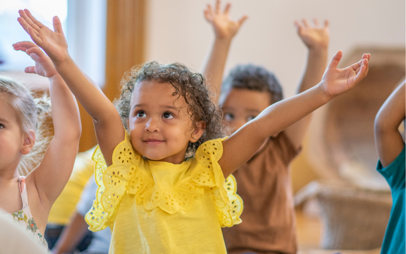 Young children in classroom raising their hands