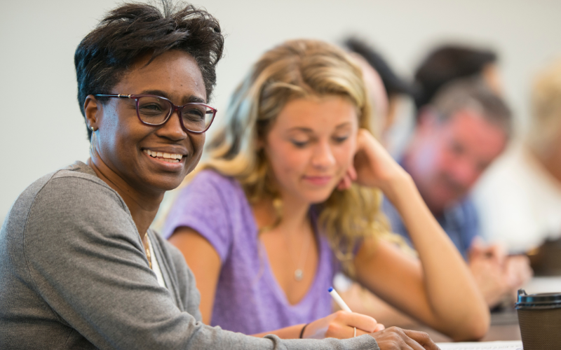 Two women in the forefront taking notes and one is smiling at the camera
