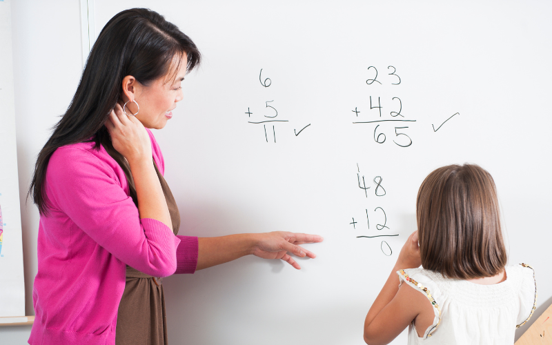Teacher and student looking at addition problems on whiteboard
