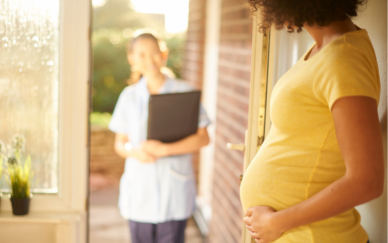 Pregnant person opening the door to their home to a person with a clipboard