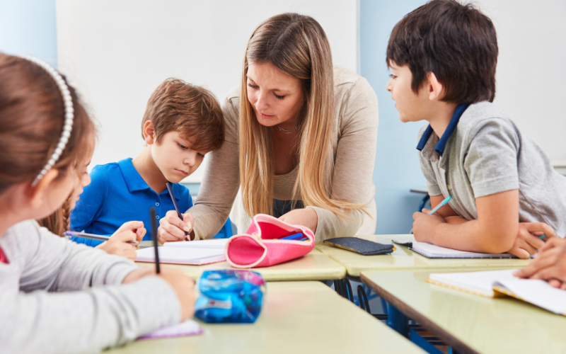 Teacher working with students at desks with notebooks and pens