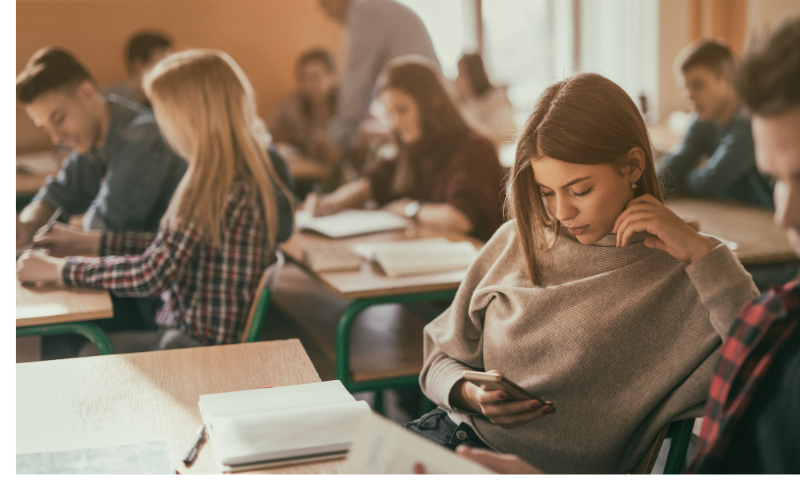 Student looking at a cell phone in a classroom of students