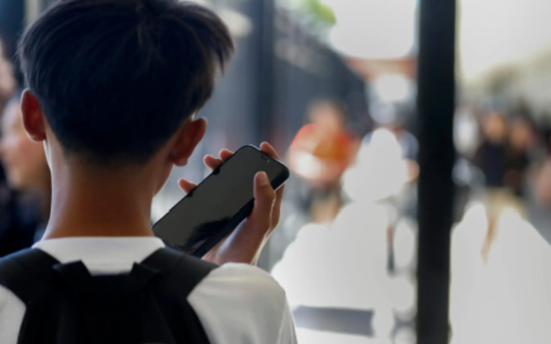 Student with backpack holding a cellphone in a school setting