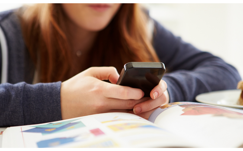student looking at a cell phone with a book in front of them