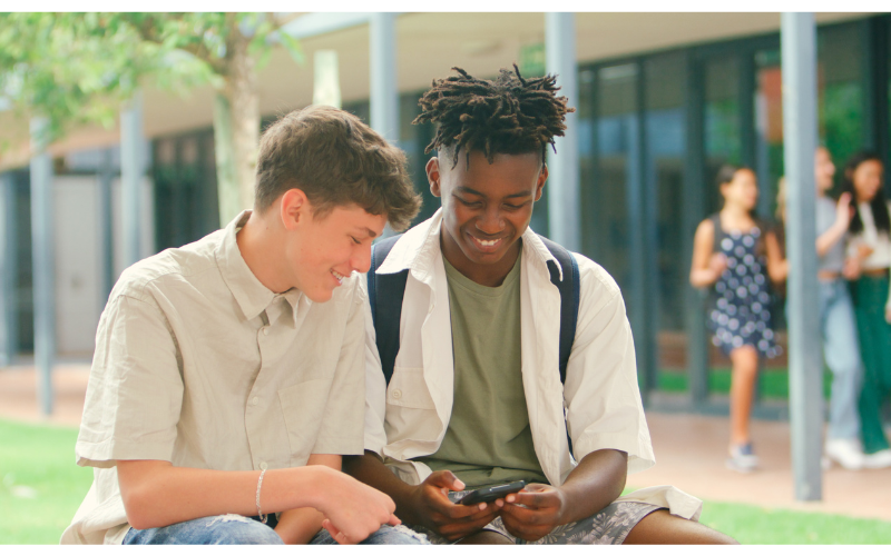 Two students looking at a phone outside of a school