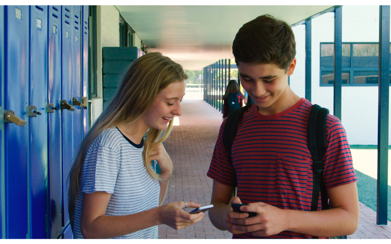 two students looking a phones near lockers
