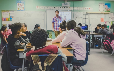 students sitting in a classroom listening to a teacher talking
