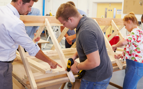 A teacher instructing students on drilling a wooden structure