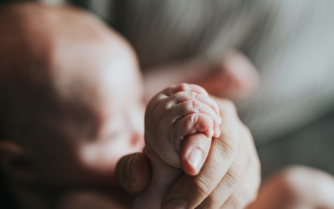a newborn's hand holding the finger of a caregiver